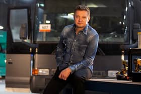 Jeremy Renner on set of Rennervations, a bus behind him and some power tools to one side (Credit: Disney+)