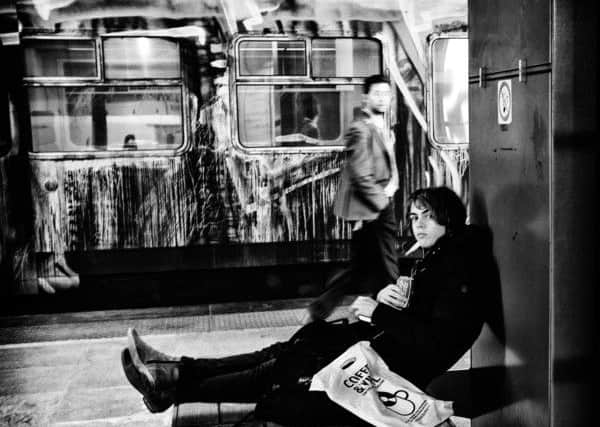 This is a very dark and atmospheric shot taken in the train station in Antwerp. The subject is androgynous and is backed by a moving figure and a train covered in graffiti.