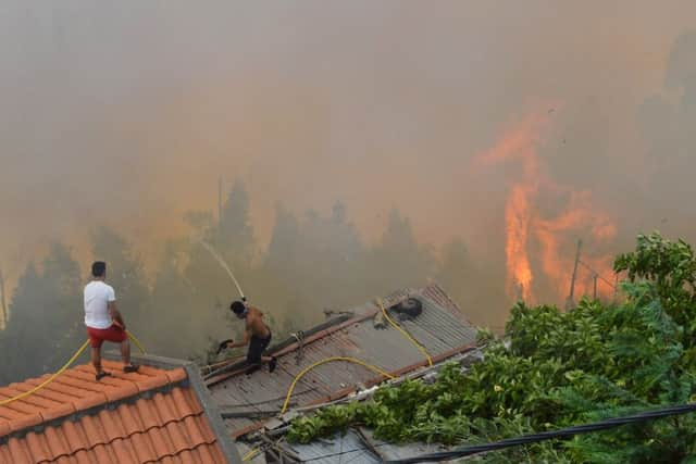 Men spray water on the roofs of houses to protect them from an approaching fire in Curral dos Romeiros, on the outskirts of Funchal, on the Madeira island, Portugal, Tuesday, Aug. 9 2016. Flames from forest fires licked at homes around Funchal, casting a smoke plume over the downtown and forcing the evacuation of more than 400 people. (AP Photo/Helder Santos)