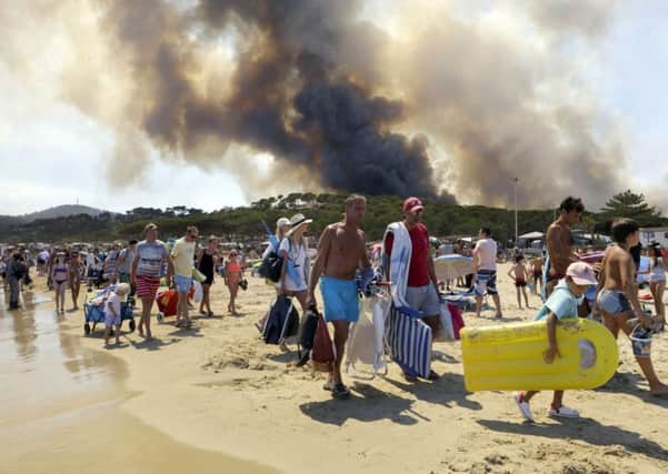 Sunbathers are being evacuated from the beach in Le Lavandou, French Riviera, as plumes of smoke rise in the air from burning wildfires, Wednesday, July 26, 2017. French authorities ordered the evacuation of up to 12,000 people around a picturesque hilltop town in the southern Cote d'Azur region as fires hopscotched around the Mediterranean coast for a third day Wednesday. (AP Photo/Claude Paris)